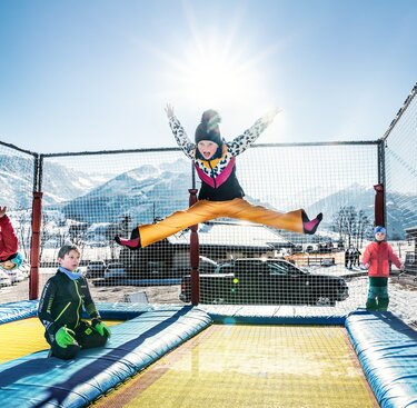 Kinder springen auf einer mit Netzen gesicherten Trampolinanlage am Erlebnisberg Naglköpfl vor verschneiten Bergen. | © TVB Piesendorf Niedernsill, Foto Harry Liebmann