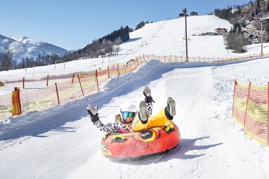 Kind mit Helm fährt in einem roten Snowtube eine präparierte, mit Fangnetzen begrenzte Schneebahn am Erlebnisberg hinunter. | © TVB Piesendorf Niedernsill, Foto Harry Liebmann