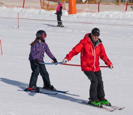 Skilehrer der Skischule Entleitner begleitet ein Kind bei einer Skiübung mit Trainingsstange. | © Florian Entleitner, Schischule Entleitner