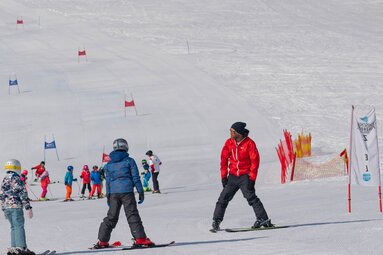 Ski instructor demonstrates an exercise to two children while other children ski between slalom gates. | © Florian Entleitner, Schischule Entleitner