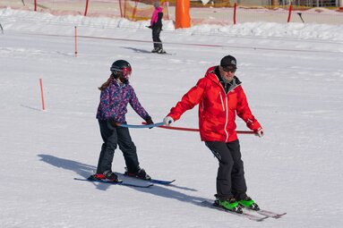Ski instructor from Skischule Entleitner assists a child during a skiing exercise using a training bar. | © Florian Entleitner, Schischule Entleitner