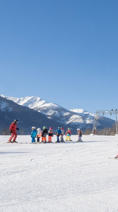 Children skiing at Erlebnisberg Naglköpfl in Piesendorf, with snow-covered slopes and mountains in the background. | © Lichtfarben