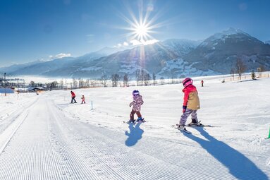 Children skiing at Erlebnisberg Naglköpfl in Piesendorf with snow-covered mountains in the background. | © Lichtfarben