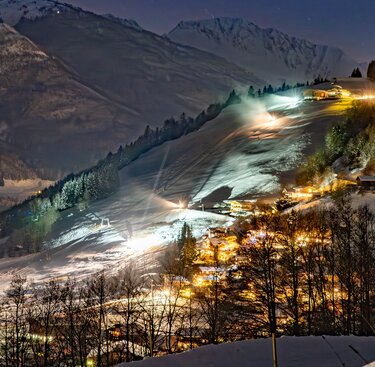 Erlebnisberg Naglköpfl bei Nacht mit beleuchteten Schneehängen und Gebäuden in der winterlichen Berglandschaft. | © TVB Piesendorf Niedernsill, Foto Lichtfarben 