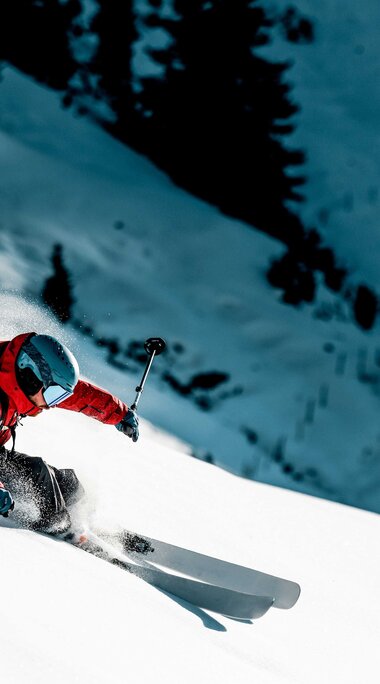 Skier in red winter clothing skiing through deep snow at KitzSki. | © e3 Media House, Max Dräger