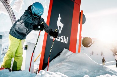 Skier with ski poles at a KitzSki facility against a snow-covered mountain backdrop. | © e3 Media House, Max Dräger