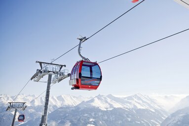 Red Panoramabahn Kitzbüheler Alpen cable car cabin in front of snow-covered mountain peaks. | © KitzSki, Werlberger