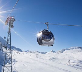 Cable car at Kitzsteinhorn above snow-covered ski slopes and mountains under a blue sky. | © Kitzsteinhorn, Foto Franz Reifmüller