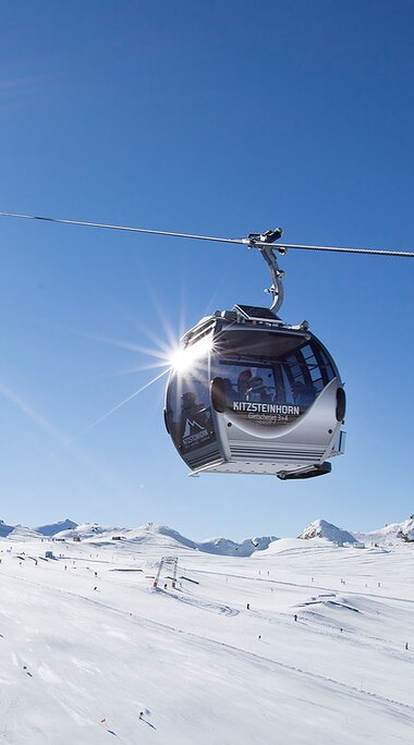 Cable car at Kitzsteinhorn above snow-covered ski slopes and mountains under a blue sky. | © Kitzsteinhorn, Foto Franz Reifmüller
