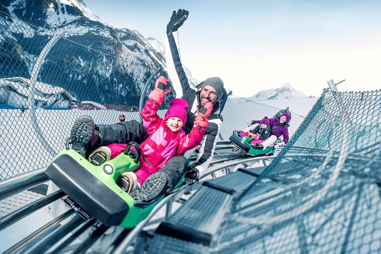 Child and adult riding an alpine coaster together through a snow-covered mountain landscape. | © Kitzsteinhorn