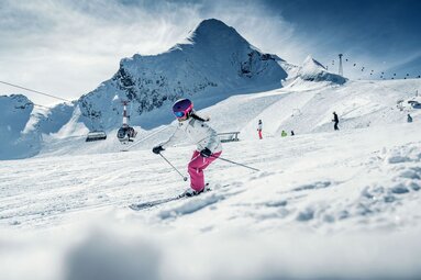 Skier on a snow-covered slope at Kitzsteinhorn, with other winter sports enthusiasts and ski lifts in the background. | © Kitzsteinhorn
