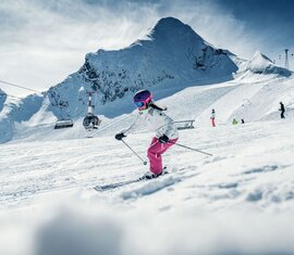 Skifahrerin auf einer verschneiten Piste am Kitzsteinhorn, im Hintergrund weitere Wintersportler und Liftanlagen. | © Kitzsteinhorn