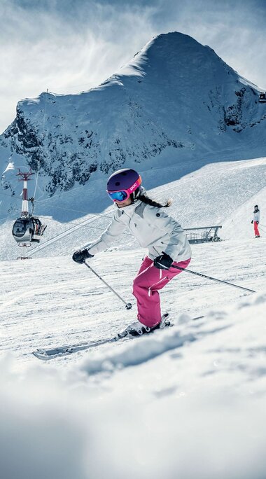Skifahrerin auf einer verschneiten Piste am Kitzsteinhorn, im Hintergrund weitere Wintersportler und Liftanlagen. | © Kitzsteinhorn