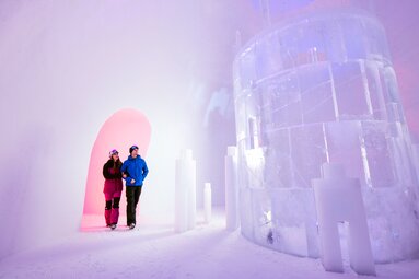 Two people among ice installations in a snow room illuminated with pink and purple light at Kitzsteinhorn. | © Kitzsteinhorn