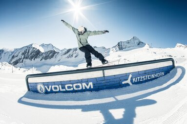 Snowboarder rides a rail in the snowpark at Kitzsteinhorn, with snow-covered mountains in the background. | © Kitzsteinhorn
