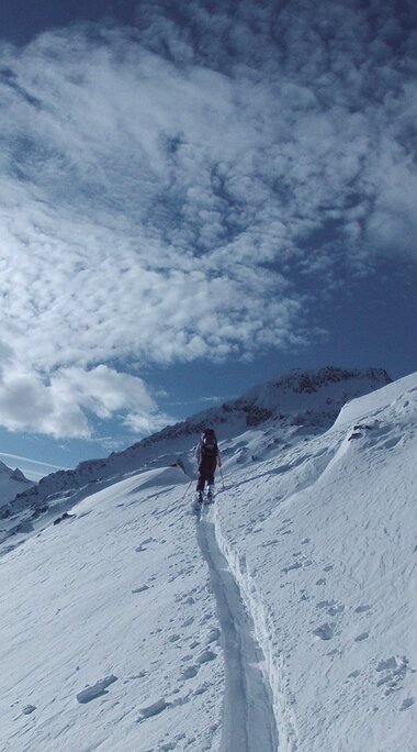 Ski tourer ascends a track across a snow-covered mountain slope at the Kitzsteinhorn. | © Stephan Obenaus