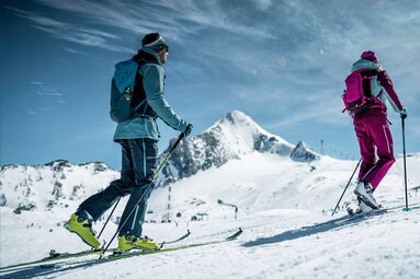 Two ski tourers ascend with touring skis and poles through the snow-covered mountain landscape at Kitzsteinhorn. | © Kitzsteinhorn