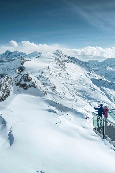 Two people on a viewing platform overlooking snow-covered peaks at Kitzsteinhorn. | © Kitzsteinhorn