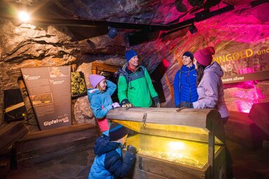 Family viewing an illuminated chest in an exhibition about Tauern gold and silver at Kitzsteinhorn. | © Kitzsteinhorn