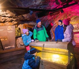 Familie betrachtet eine beleuchtete Truhe in einer Ausstellung über Tauerngold und -silber am Kitzsteinhorn. | © Kitzsteinhorn
