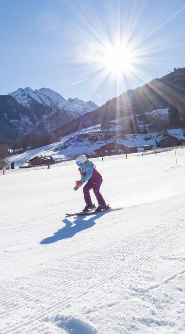 Child skiing in sunshine on the groomed slope at Bärnbachlift with snow-covered mountains behind. | © Lichtfarben