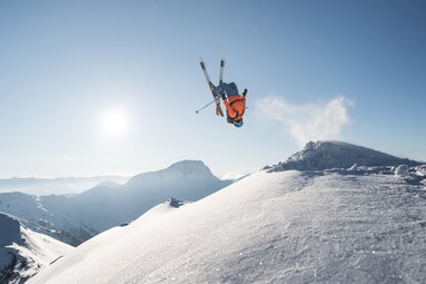 Freeride-Skifahrer bei einem Sprung über einem verschneiten Berghang in Saalbach, im Hintergrund liegt eine alpine Berglandschaft. | © saalbach.com, Moritz Ablinger