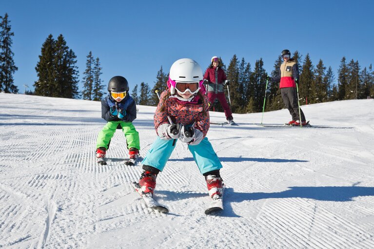 Zwei Kinder fahren Ski im Skicircus Saalbach Hinterglemm Leogang Fieberbrunn, zwei Erwachsene stehen hinter ihnen. | © Skizirkus Saalbach Hinterglemm Leogang Fieberbrunn, Foto Mirja Geh