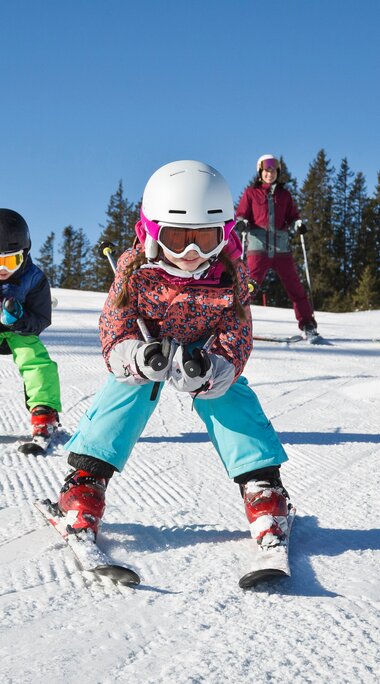 Zwei Kinder fahren Ski im Skicircus Saalbach Hinterglemm Leogang Fieberbrunn, zwei Erwachsene stehen hinter ihnen. | © Skizirkus Saalbach Hinterglemm Leogang Fieberbrunn, Foto Mirja Geh