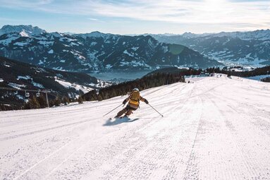 Skifahrer auf einer Piste der Schmittenhöhe mit Blick auf den Zeller See und die verschneiten Berge. | © Schmittenhöhebahn AG, Foto Johannes Radlwimmer