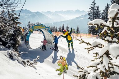 Zwei Kinder auf Ski mit Drachenmaskottchen am Eingang zu Schmidolins Drachenpark auf der Schmittenhöhe. | © Schmittenhöhebahn AG