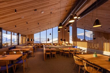 Innenraum des Panoramarestaurants Franzl mit Holzmöbeln und großen Fenstern mit Blick auf verschneite Berge. | © Schmittenhöhebahn AG