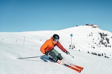 Skier descends a groomed slope with the snow-covered summit of Schmittenhöhe in the background. | © Schmittenhöhebahn AG