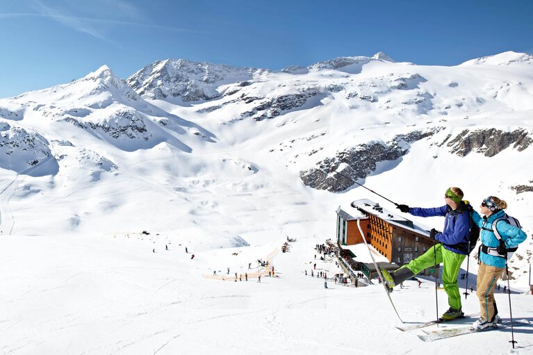 Two skiers overlooking ski slopes and snow-covered mountains at Weißsee Gletscherwelt near Uttendorf. | © Weißsee Gletscherwelt