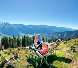 Drei Personen bei einer Wanderpause am Hochsonnberg mit Blick über das Tal auf die umliegenden Berge. | © TVB Piesendorf Niedernsill, Foto Harry Liebmann 