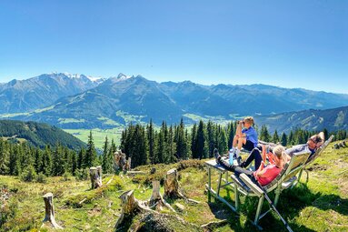 Drei Personen bei einer Wanderpause am Hochsonnberg mit Blick über das Tal auf die umliegenden Berge. | © TVB Piesendorf Niedernsill, Foto Harry Liebmann 