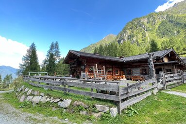 Schaunbergalm im Mühlbachtal bei Niedernsill mit Holzhütte, Sitzbänken und Zaun vor bewaldeten Berghängen. | © TVB Piesendorf Niedernsill