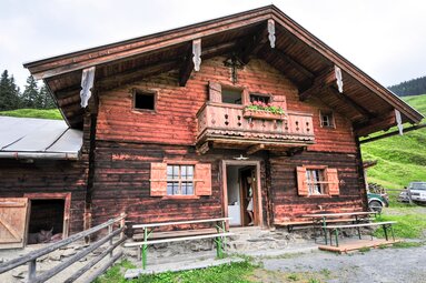 Katzsteinalm mit Holzhütte, Balkon und Sitzbänken auf einer grünen Almfläche. | © TVB Piesendorf Niedernsill
