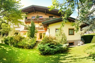 Haus Wegscheider with wooden balconies and flowers, surrounded by a garden with trees and shrubs. | © TVB Piesendorf Niedernsill, Foto Harry Liebmann