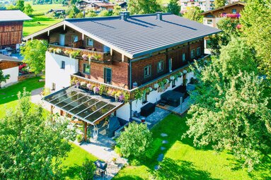 Göpplerbauer with timber façade, flower-lined balconies and garden in Piesendorf-Niedernsill, seen from above. | © Göpplerbauer