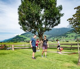 Familie mit zwei Kindern an einer Slackline auf einer Wiese, im Hintergrund Fahrräder und eine alpine Tallandschaft. | © TVB Piesendorf Niedernsill, Foto Lichtfarben
