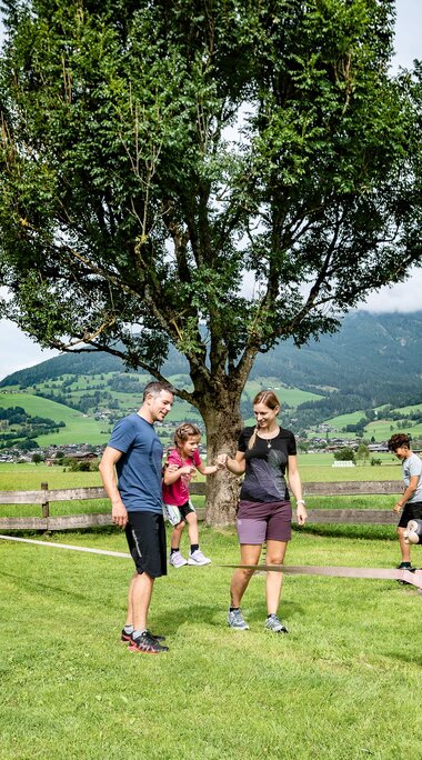 Family with two children at a slackline on a meadow, with bicycles and an Alpine valley in the background. | © TVB Piesendorf Niedernsill, Foto Lichtfarben