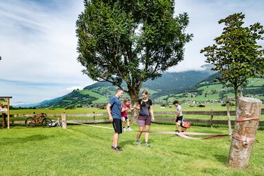 Family with two children at a slackline on a meadow, with bicycles and an Alpine valley in the background. | © TVB Piesendorf Niedernsill, Foto Lichtfarben