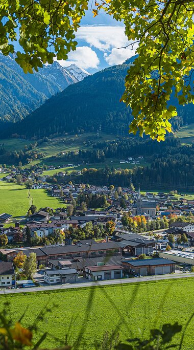 Blick auf Niedernsill im Herbst mit Kirche, Häusern und grünen Wiesen. Im Hintergrund bewaldete Berghänge und Berggipfel. | © TVB Piesendorf Niedernsill, Brcina Photography