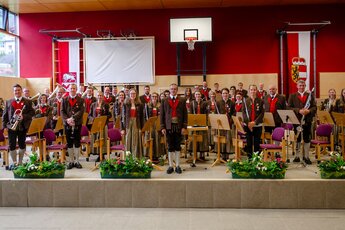 Mitglieder der Trachtenmusikkapelle Piesendorf stehen in Tracht mit ihren Blasinstrumenten und Notenpulten auf einer Bühne. | © TMK Piesendorf
