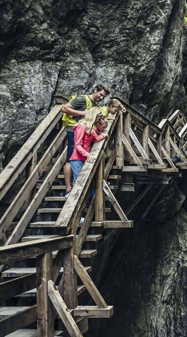 A family stands on a wooden walkway in Sigmund Thun Gorge in Kaprun, looking at the waterfall. | © Zell am See-Kaprun Tourismus