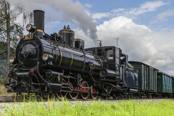 Black steam locomotive of the Pinzgau Local Railway pulling historic green carriages, with smoke rising from the chimney. | © Salzburg AG