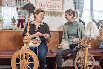 Two women sit at spinning wheels and process sheep’s wool into yarn. | © Lichtfarben