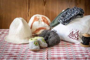 Felt hats, small felt shoes, wool and knitted handicrafts are arranged on a checkered table. | © Lichtfarben