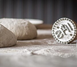 Bemehlte Brotteiglinge liegen neben einem Brotstempel auf einer Arbeitsfläche und sind zum weiteren Verarbeiten vorbereitet. | © Lichtfarben