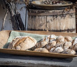 Floured loaves and small bread rolls in a wooden trough in front of an old wooden barrel. | © Lichtfarben